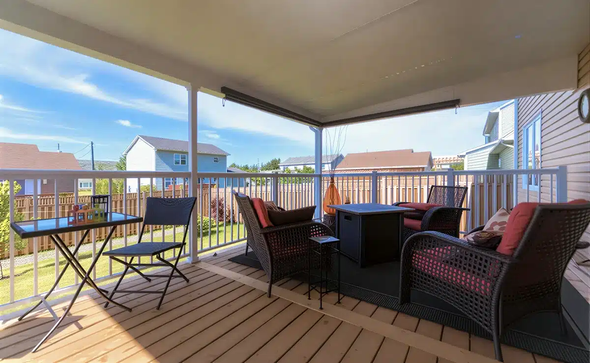 A residential wooden deck featuring white aluminum picket railings and a protective patio cover overlooking a backyard.