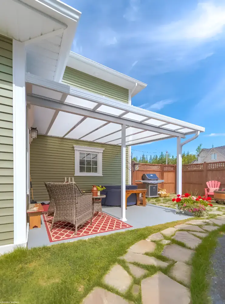 A white-framed acrylic patio cover installed over a concrete patio with a hot tub and seating area, attached to a green-sided house.