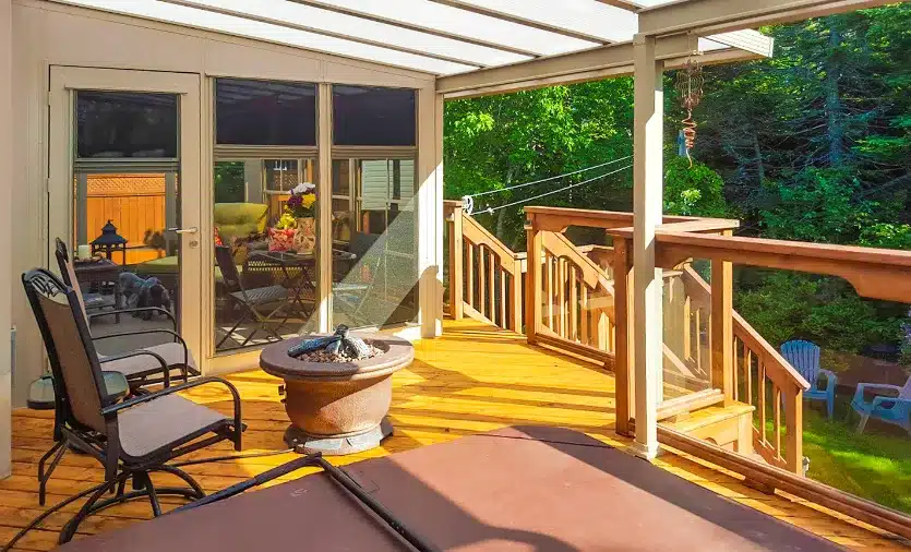 A white-framed acrylic patio roof sheltering a dark blue hot tub and outdoor lounge area on a grey concrete pad.