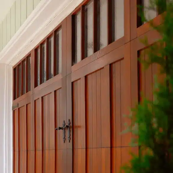 Close-up of a warm wood-toned carriage garage door with vertical panels and decorative black hardware.