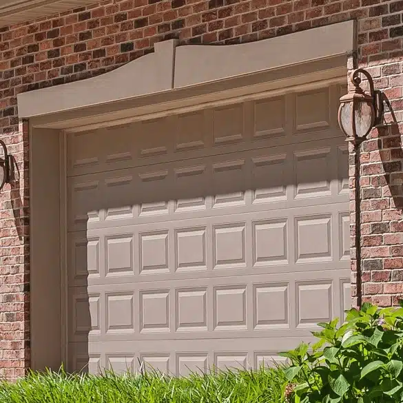 A single tan raised-panel garage door set into a red brick wall with a decorative arch lintel and an outdoor carriage light.