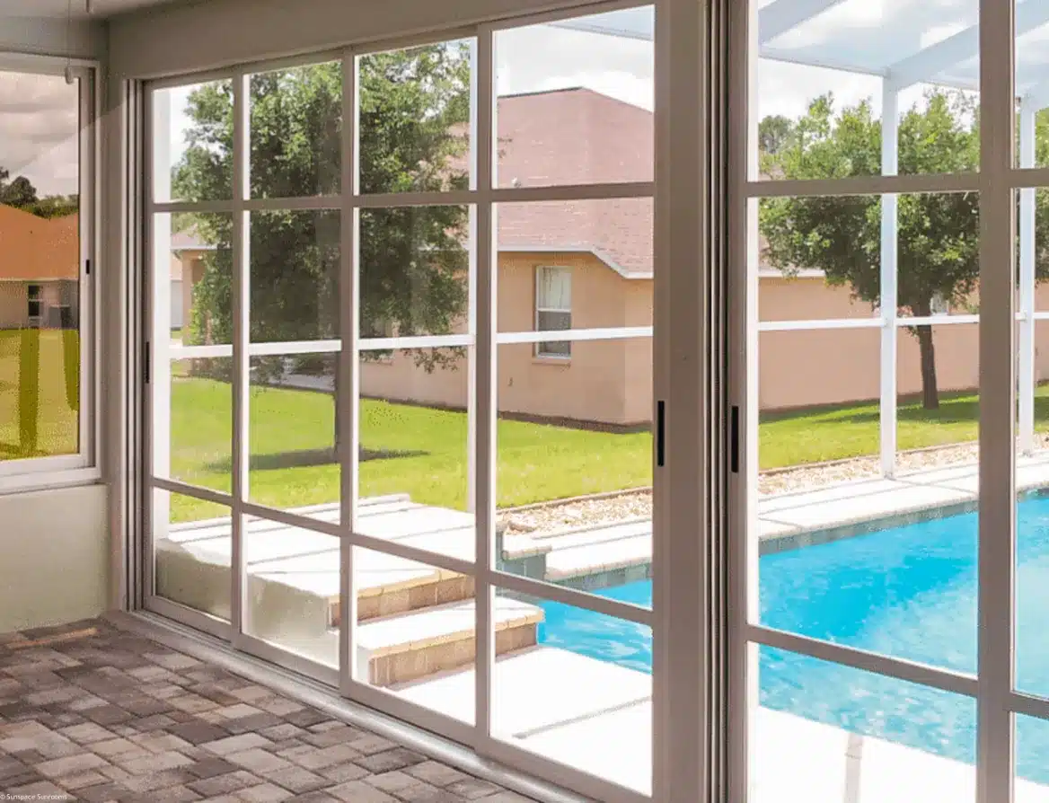 Interior view of a sunroom featuring WeatherMaster H4T vertical 4-track vinyl windows with white frames and integrated screens, looking out onto a backyard swimming pool and patio.