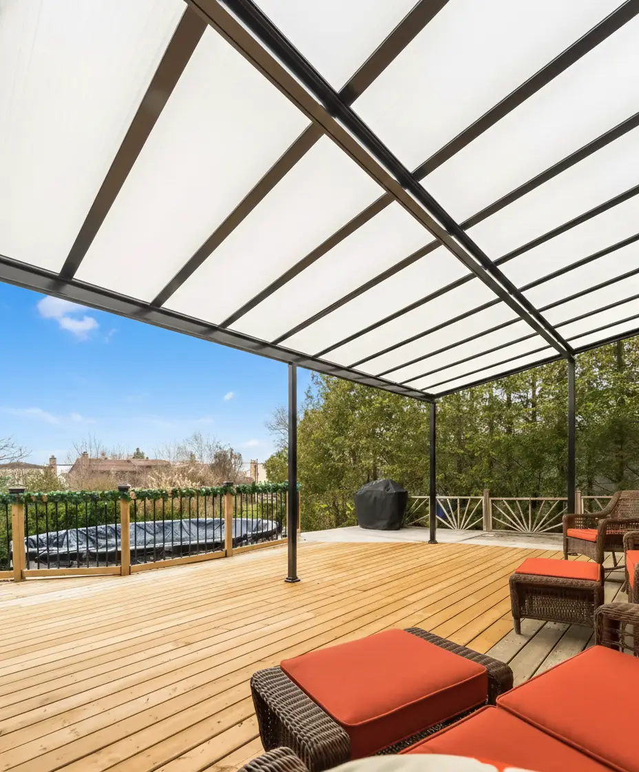 A wooden deck with orange cushions under a black-framed acrylic patio cover with translucent panels.